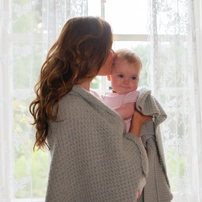 Mother holding baby wearing family blanket in Seasong 